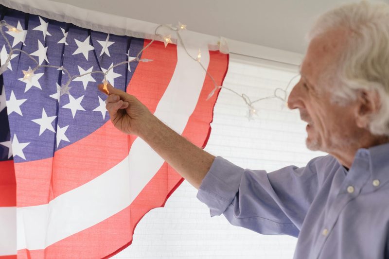 Senior adult decorating indoors with an American flag and string lights for a festive celebration.