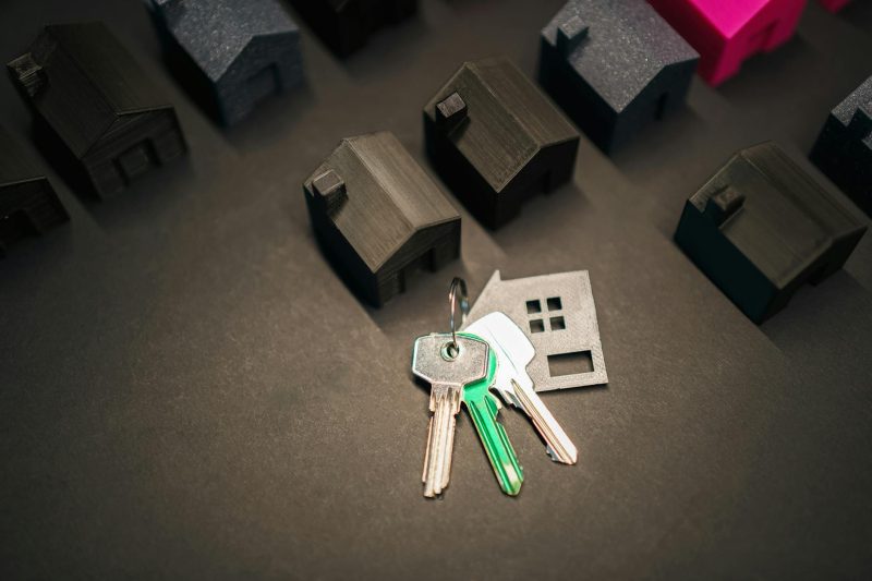 Miniature house models arranged with silver keys on a wooden surface.