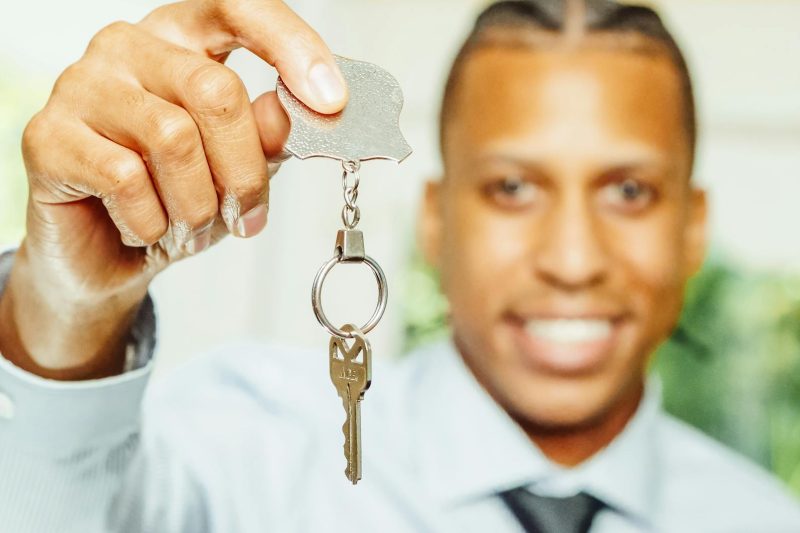 Cheerful real estate agent holding a house key, smiling in a bright, welcoming office setting.
