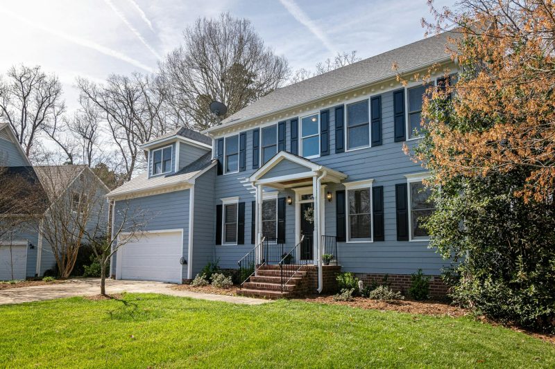 Spacious blue family home with garage, set among trees and lush lawns in a suburban neighborhood.