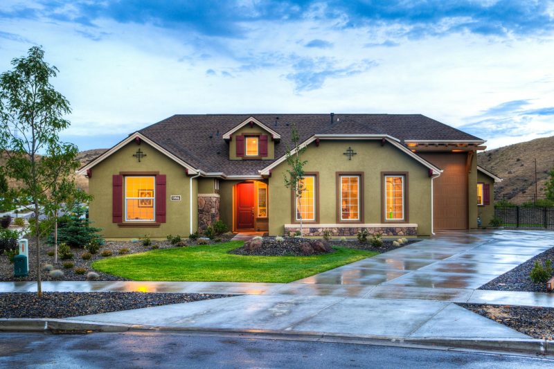 Modern home exterior with illuminated architecture, lush green lawn, and a wet driveway.