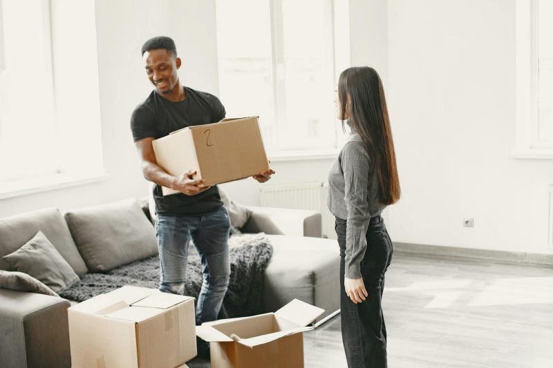 Happy couple joyfully carrying boxes into a bright, sunlit new home.