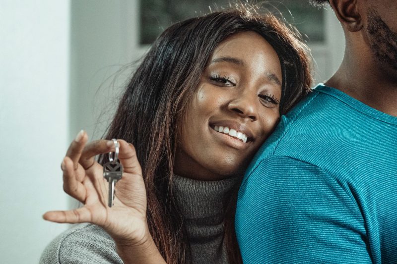 Joyful couple celebrating their new home, holding a set of house keys in a sunny outdoor setting.