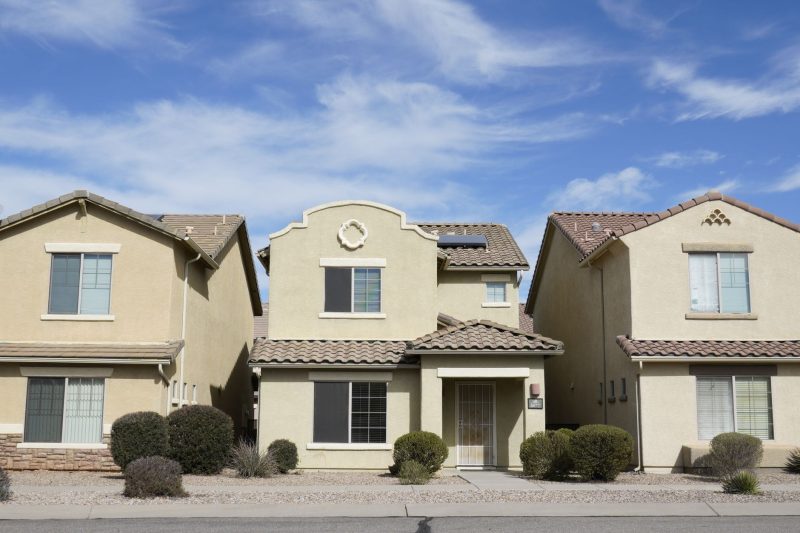 Three adjacent houses in a Tucson, Arizona suburban neighborhood under a clear blue sky.