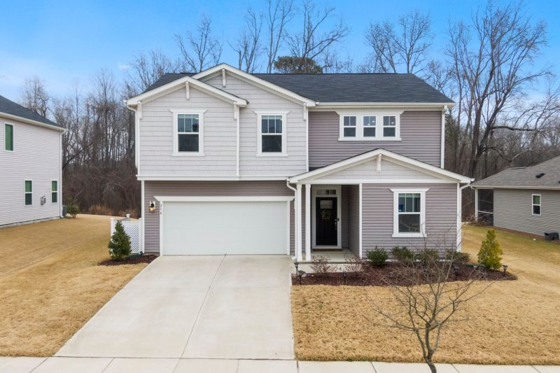 Charming two-story suburban home with a garage surrounded by green lawn and trees in Fuquay-Varina, NC.