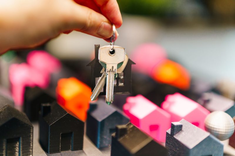 Colorful miniature houses with a hand holding a set of keys, symbolizing real estate decisions.